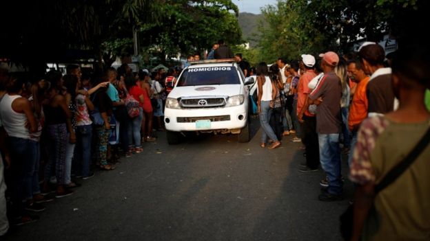 Homicide unit police car arrives at scene of prison fire, surrounded by relatives