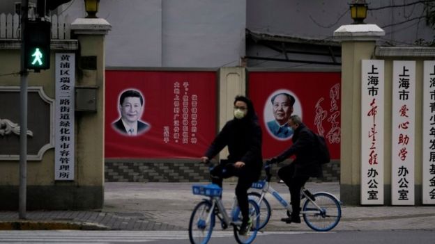 Gente con mascarillas pasando al lado de retratos de Xi Jinping y de Mao Zedong.