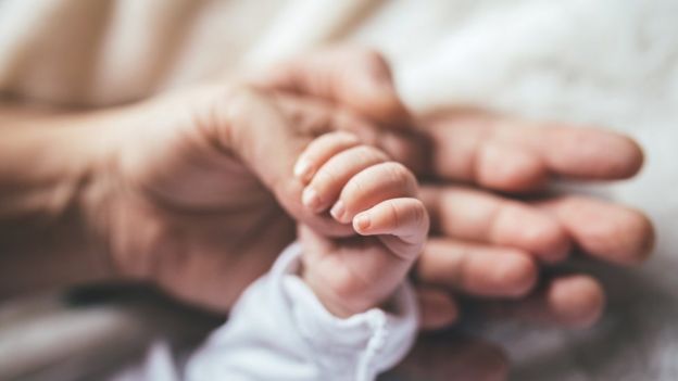 рука взрослого держит руку новорожденного ребенка