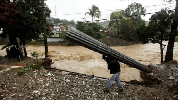 Hombre carga un techo de calamina frente a un río desbordado