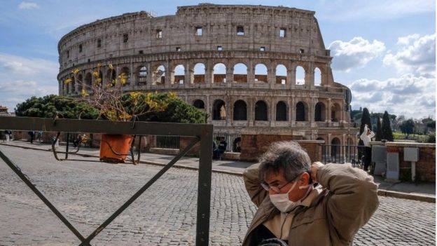 A tourist wearing a mask sits at the tables of a restaurant in front of the Colosseum, in Rome, Italy, 9 March 2020.