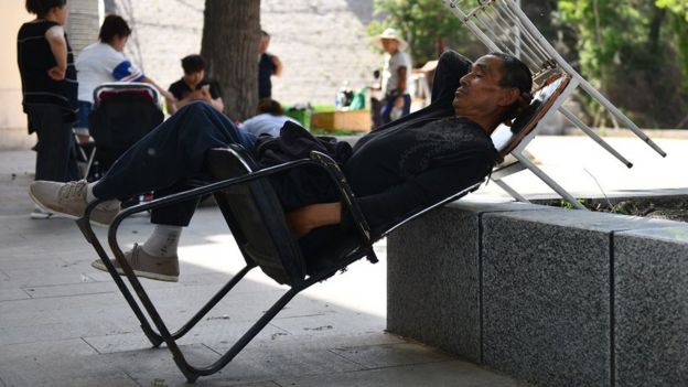 A Chinese man is having a nap on a chair, in a public square