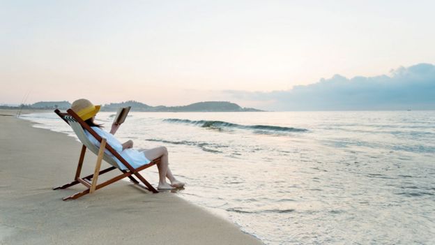 Mujer leyendo sentada frente al mar