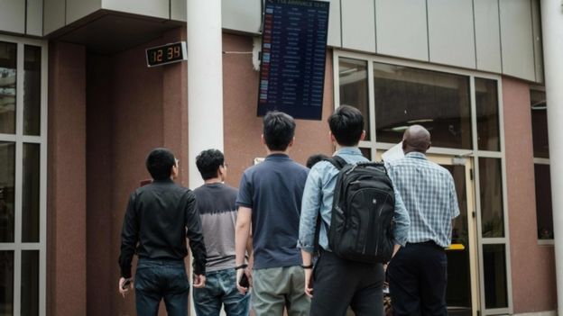 Image shows a group looking as the arrival schedule board at Nairobi airport