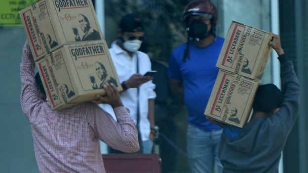 Two men carry boxes of liquor