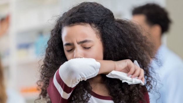 A teenager coughing into her elbow
