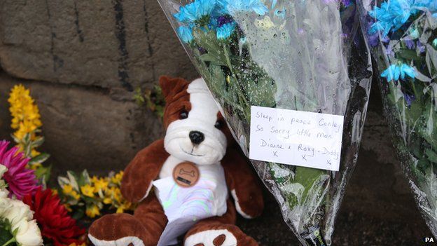 Floral tributes and a teddy laid by a wall