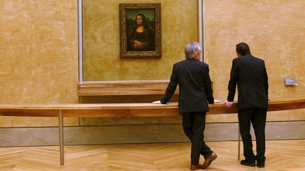 Two men look at the Mona Lisa at the Louvre Museum in Paris