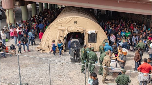 Border Patrol agents, including members of U.S. Border Patrol's BORSTAR teams (in tactical uniforms) provide food, water and medical screening to scores of migrants at a processing centre