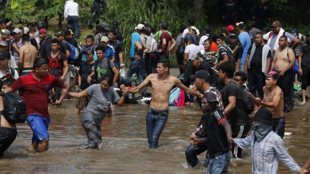 Mostly Honduran migrants cross a river that separates Guatemala and Mexico on 29 October 2018