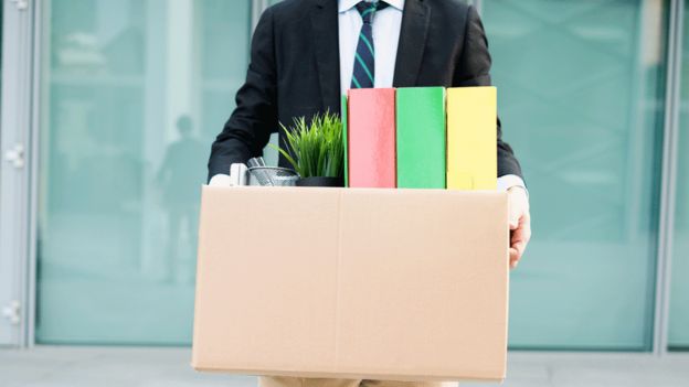 Homem deixando escritório com pertences dentro de uma caixa