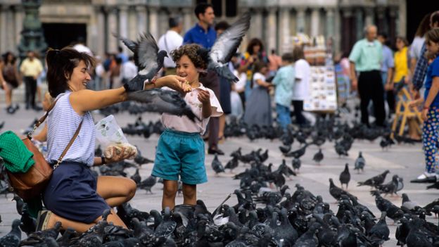 Mulher e criança dando de comer a pombos em uma praça