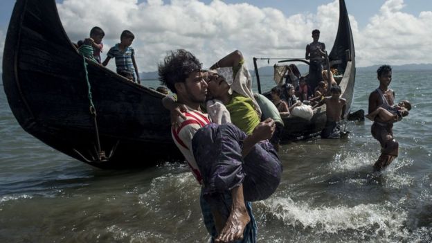 Bangladeshi man helps Rohingya Muslim refugees to disembark from a boat on the Bangladeshi shoreline of the Naf river after crossing the border from Myanmar in Teknaf on 30 September 2017
