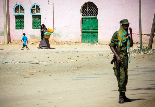 A Somali woman and child walk along a street as a fighter of the pro-government Ras Kimboni Brigade stands guard in the centre of the southern Somali port city of Kismayo adjacent to the old police station while a combat engineering team inspects the surrounding area following reports of a suspected improvised explosive device (IED) left behind by the al-Qaeda-affiliated extremist group al-Shabaab.