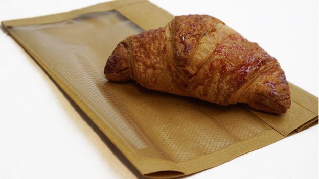 Um Croissant em um saco de padaria com a alternativa para plástico em cima