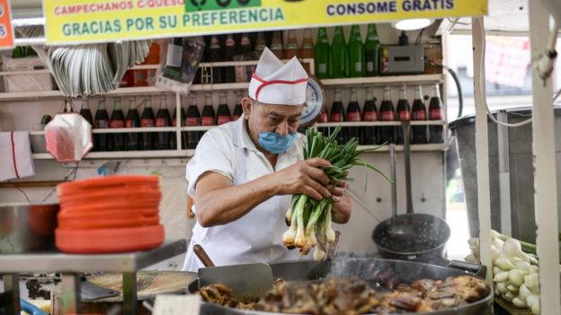 Cozinheiro manipula vegetais com máscara em barraca de comida no México