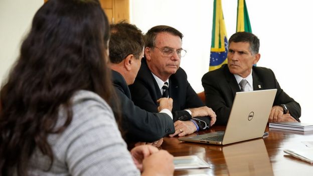 Bolsonaro e Santos Cruz sentados à mesa diante de laptop em reunião