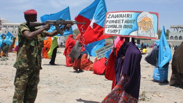 Um soldado da Somália aponta sua arma para um poster com o rosto do líder da Al-Qaeda durante um protesto contra o Al-Shabab em 2014