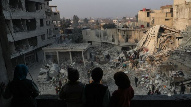 Children look out from their destroyed home as rescue workers search for survivors after air strikes destroyed residential buildings in Hamouria city, in the besieged rebel-held Eastern Ghouta, Syria (9 January 2018)