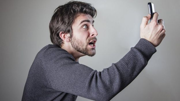 Un hombre mira a su teléfono enojado