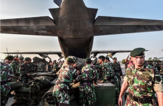 Indonesian soldiers load emergency supplies into a Hercules military plane before heading to Palu