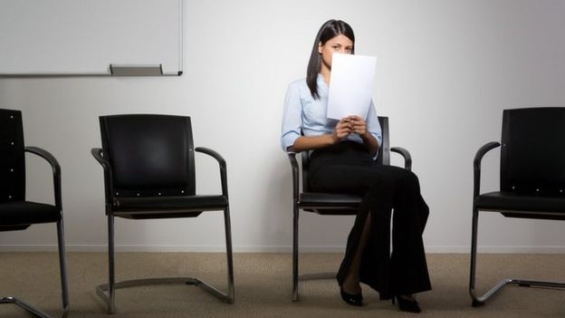 Una personas sentada, cubriéndose el rostro con unos papeles