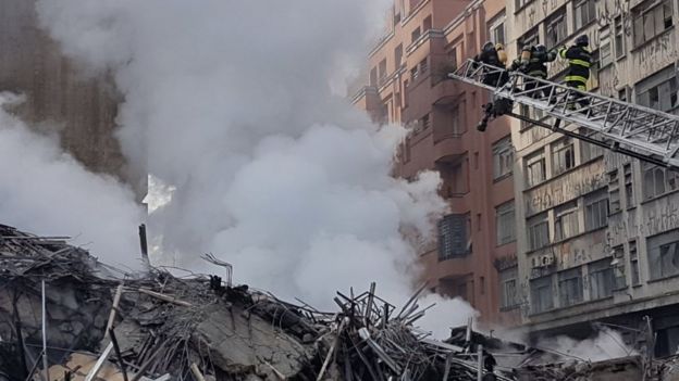 Bombeiros tentam controlar incêndio nos escombros do prédio