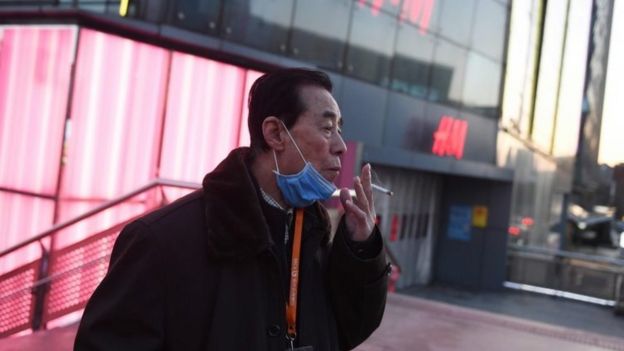 A man lowers his face mask to smoke a cigarette in Beijing on February 17, 2020