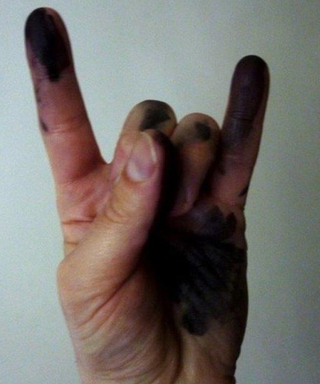 Hand covered in ink making the rock sign with little finger and pointer finger in air