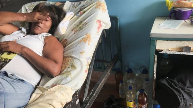 Una mujer en una cama de hospital con botellas de agua en el piso