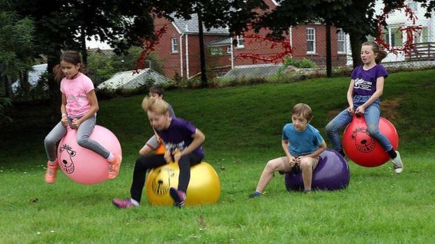 Children race on bouncy hoppers along a grassy field