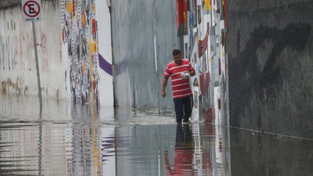 Homem andando em rua lagada após temporal em São Paulo