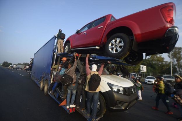 Migrantes trepan a un tráiler con autos nuevos