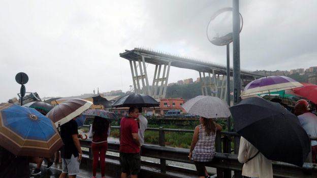 People gather to watch the rescue operation after a section of a giant motorway bridge collapsed, on August 14, 2018 in Genoa