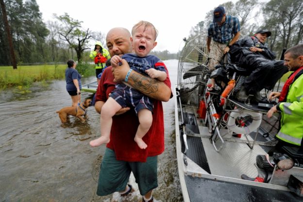 Imagem mostra embarcação, seis adultos, um cachorro e um bebê nos braços de um homem em área inundada na Carolina do Norte, após a passagem do furacão Florence.