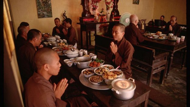 Monjes budistas oran antes de comer. frente a ellos un despliegue de platillos