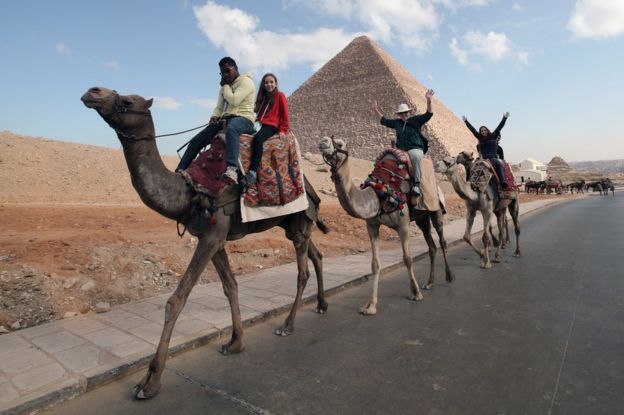 Tourists ride on camels in front of the Giza Pyramids, in Giza, Egypt, 26 December 2018