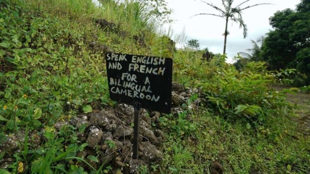 A sign saying " Speak English or French for a bilingual Cameroon" outside a now abandoned school on May 22, 2019 in a rural part of SW Cameroon