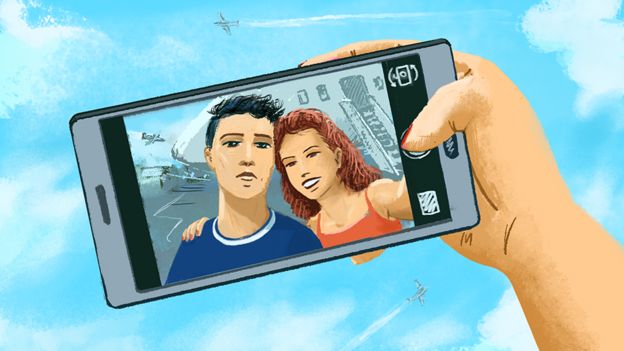 Uma mão segura um telefone celular, mostrando uma imagem de um casal.