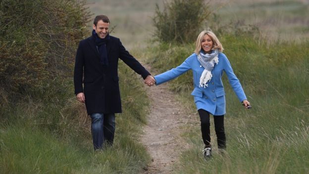 Macron and Trogneux walking on a grassy hillock