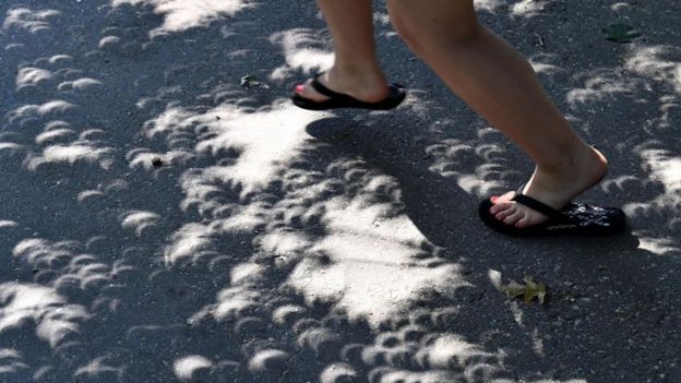 Pies sobre sombras en forma de media luna creadas por el eclipse solar.