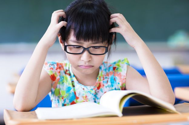 A little girl looking at an open book, with an unhappy expression on her face