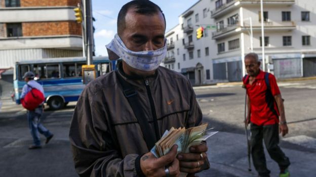 Un hombre contando un fajo de billetes con una mascarilla de tela.