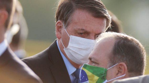 Bolsonaro olha para baixo de máscara, cercado por assessores, em área externa