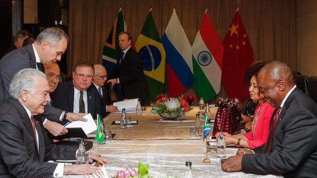 Em encontro bilateral, imagem mostra Michel Temer sentado em frente ao presidente da África do Sul, Cyril Ramaphosa, com ministros e outras pessoas à mesa, durante cúpula dos Brics, em Joanesburgo.