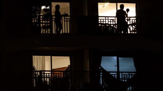 Sombras de duas pessoas em apartamentos diferentes batendo panela da varanda