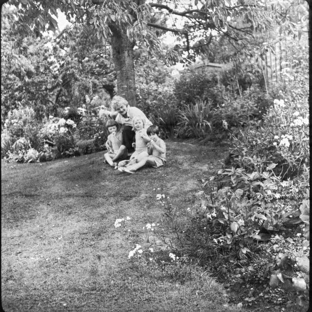 Black and white photo of three children and adult in garden