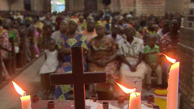 People sit in church with a cross and candles in the foreground