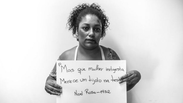 Mulher segurança placa com letra de Noel Rosa: "Mas que mulher indigesta, merece um tijolo na testa"