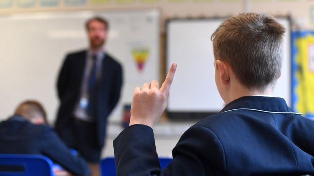 child in a classroom putting his hand up to ask a question